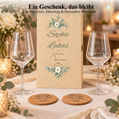 Weinglas-Geschenkset mit Namen, floral bedruckter Holzbox und Korkuntersetzern auf einem Tisch bei Kerzenlicht.