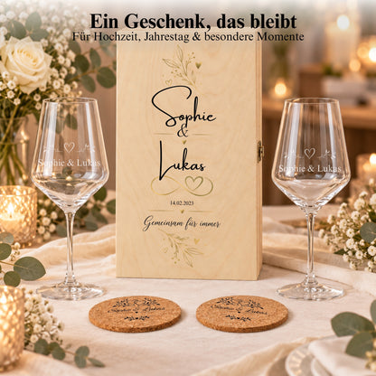 Weinglas-Geschenkset mit Namen, floral bedruckter Holzbox und Korkuntersetzern auf einem Tisch bei Kerzenlicht.