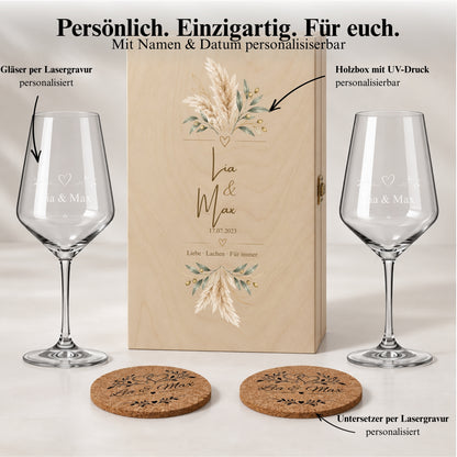 Weinglas-Geschenkset mit Namen, floral bedruckter Holzbox und Korkuntersetzern auf einem Tisch bei Kerzenlicht.