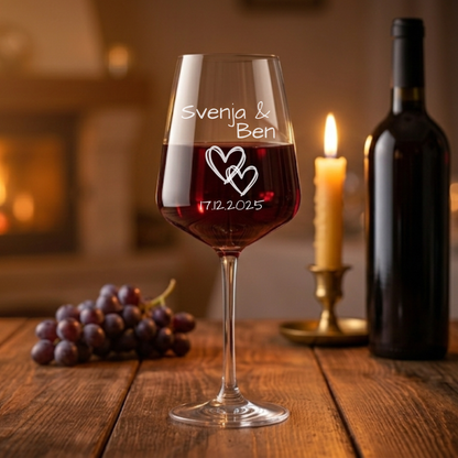 Personalisiertes Rotweinglas mit Gravur „Alina & Björn“, Herzmotiv und Datum 17.12.2025 auf rustikalem Holztisch mit rotem Wein, Kerzenlicht und gemütlicher Hintergrundbeleuchtung – romantisches Geschenk zur Hochzeit oder zum Jahrestag.