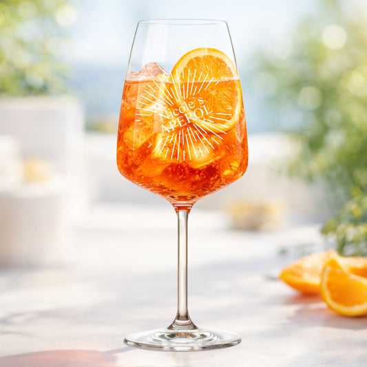 Hand hält personalisiertes Aperol Spritz Glas mit Sunburst-Gravur und Namen Nicole – sommerliche Gartenparty
